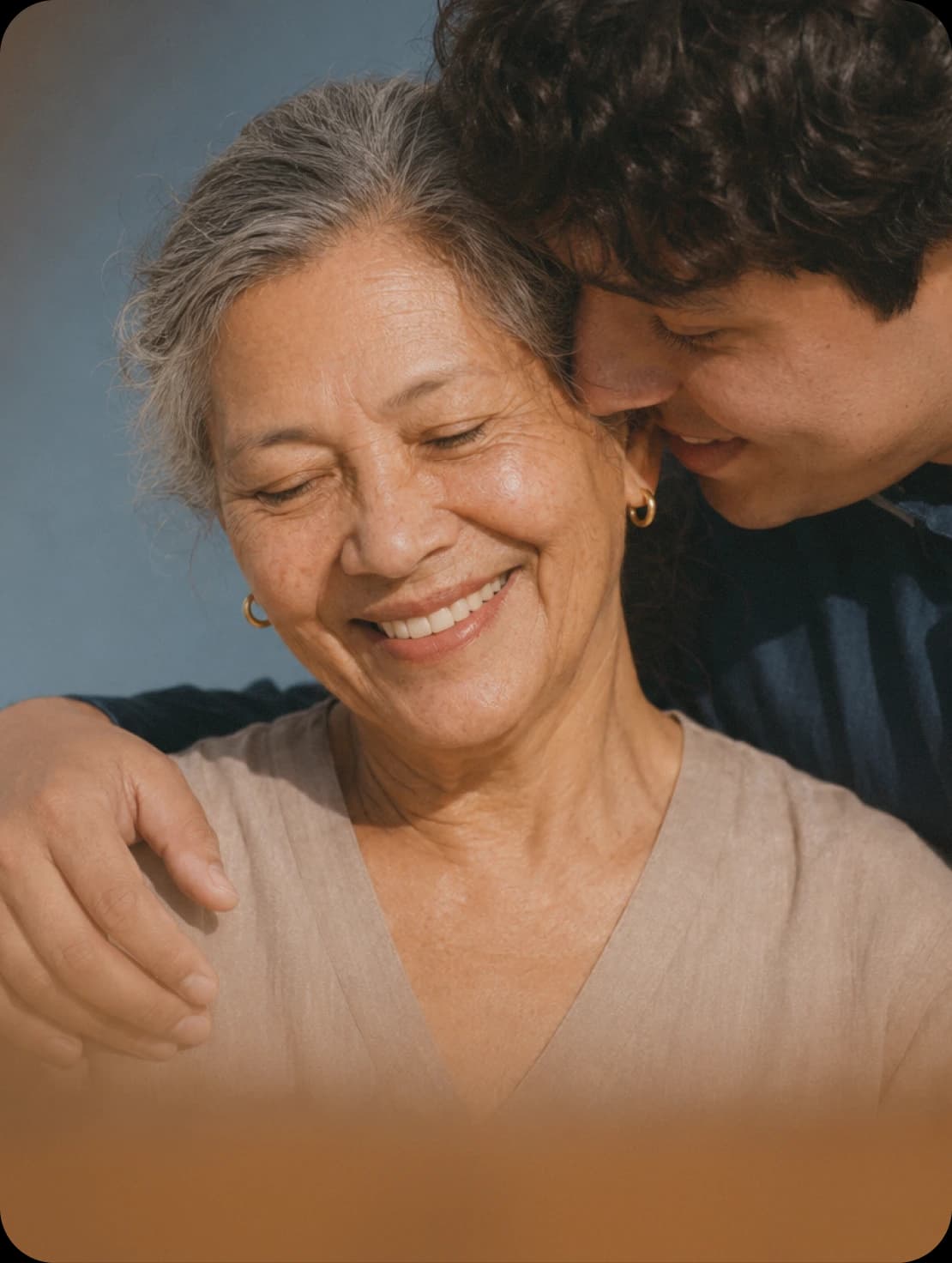 A young man hugging his mother from behind, both of them smiling