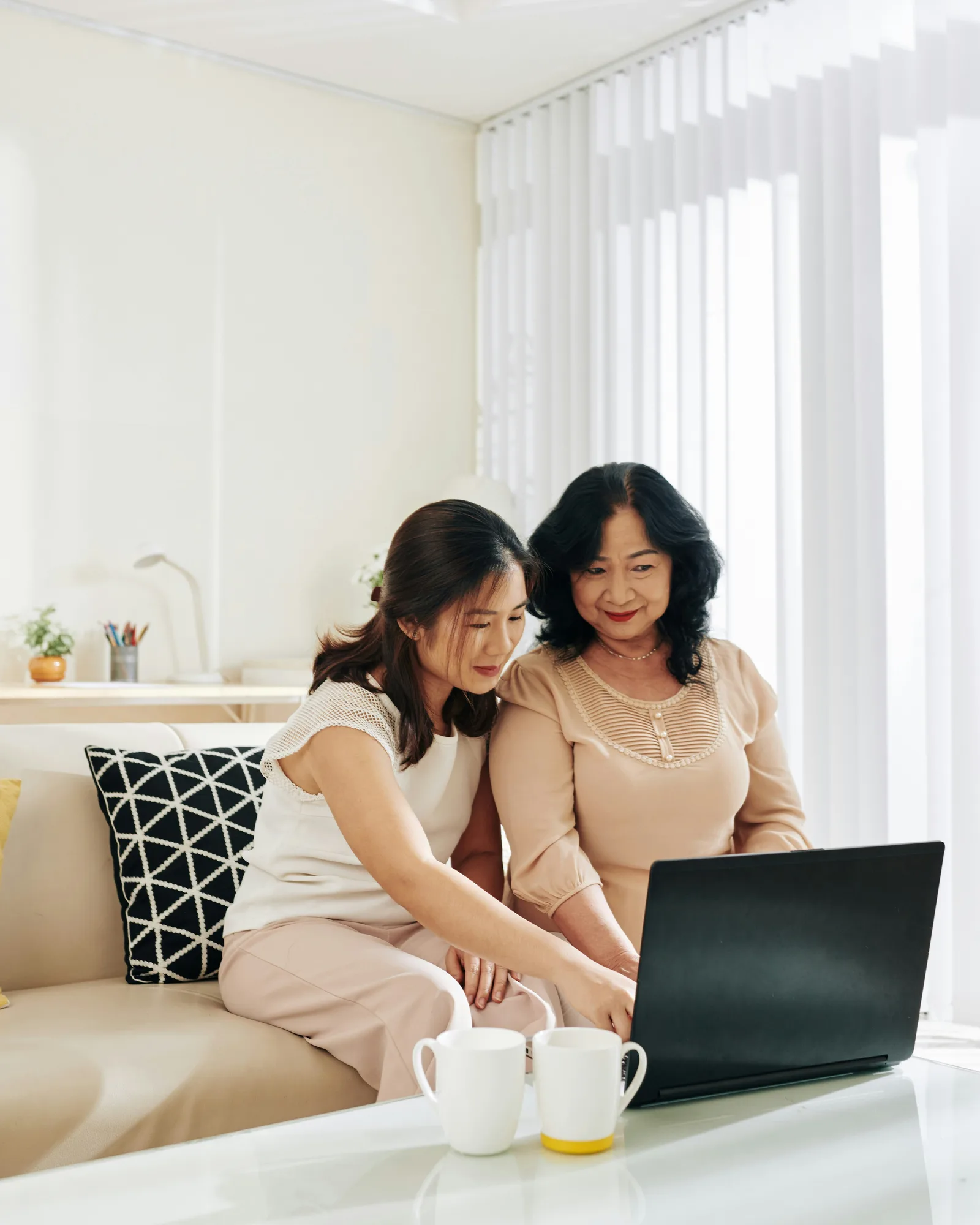 A woman and her adult daughter side by side on a sofa, looking at a laptop together
